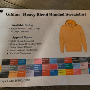 以下が含まれることがあります： マスタードイエローのGildan Heavy Blendフード付きスウェットシャツ。画像には、利用可能なサイズ、アパレル仕様、30以上のカラーバリエーションのカラーチャートが表示されています。スタイルコードは18500、G185です。