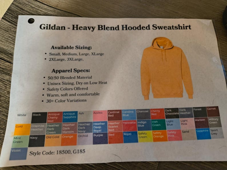 以下が含まれることがあります： マスタードイエローのGildan Heavy Blendフード付きスウェットシャツ。画像には、利用可能なサイズ、アパレル仕様、30以上のカラーバリエーションのカラーチャートが表示されています。スタイルコードは18500、G185です。