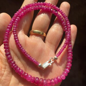 Op de afbeelding: Een ketting bestaande uit kleine, gefacetteerde, dieproze robijnkralen die aan elkaar zijn geregen. De streng is voorzien van een gepolijste, zilverkleurige karabijnsluiting aan de uiteinden voor een veilige sluiting van de kralen.