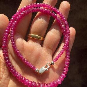 Op de afbeelding: Een ketting bestaande uit kleine, gefacetteerde, levendige magenta-roze edelsteenkralen. De streng is voorzien van een gepolijste zilverkleurige karabijnsluiting aan de uiteinden, wat zorgt voor een veilige sluiting van de cirkelvormige kralen.