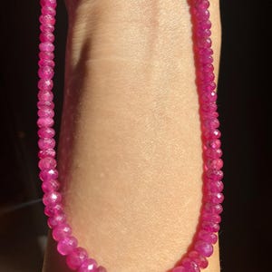 Peut inclure: Un collier de pierres précieuses rose vif. Le collier est composé de nombreuses petites pierres précieuses rondes et facettées, enfilées pour former un brin continu. Les pierres précieuses ont une couleur rose vif et saturée, et les facettes captent la lumière, créant un effet scintillant.