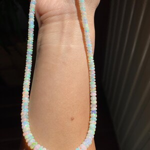 May include: A necklace made of small, iridescent opal beads. The beads show a range of colours, including white, blue, green, and pink, creating a subtle, shimmering effect. The necklace is strung together, forming a complete circle.
