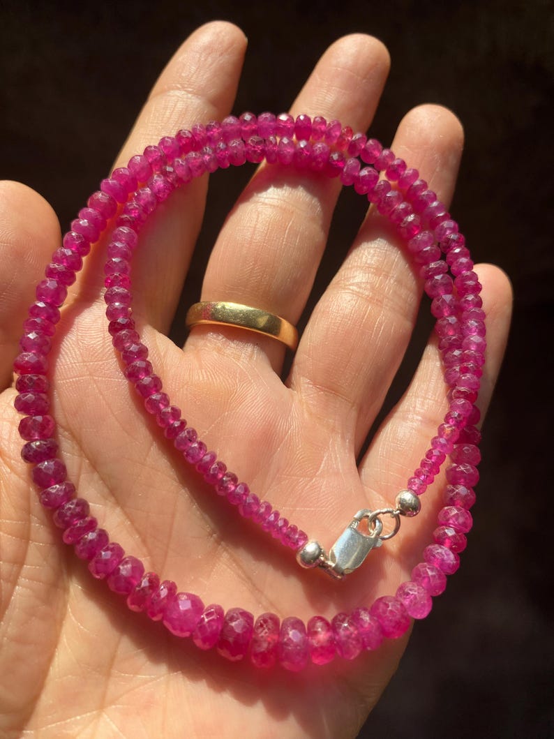 Op de afbeelding: Een ketting bestaande uit kleine, gefacetteerde, levendige magenta-roze edelsteenkralen. De streng is voorzien van een gepolijste zilverkleurige karabijnsluiting en een klein zilverkleurig kraaltje aan elk uiteinde bij de metalen sluiting.