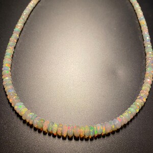 May include: A necklace featuring iridescent opal beads. The beads are a mix of white, pink, green, and orange, with a subtle sparkle. The necklace is strung together, creating a beautiful piece of jewellery. The necklace is approximately 40 cm in length.