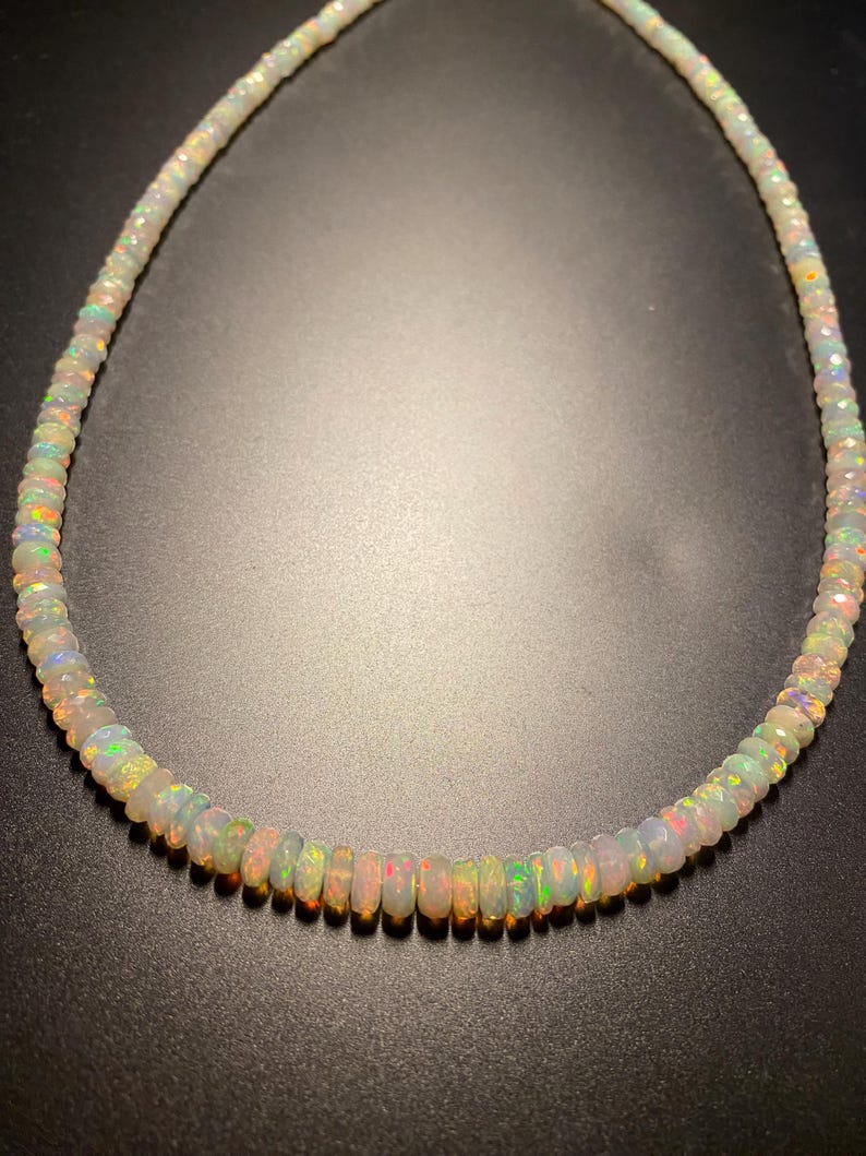 May include: A necklace featuring iridescent opal beads. The beads are a mix of white, pink, green, and orange, with a subtle sparkle. The necklace is strung together, creating a beautiful piece of jewellery. The necklace is approximately 40 cm in length.