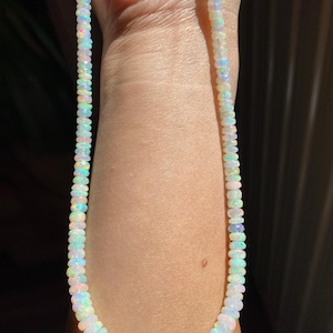 May include: A necklace made of small, iridescent opal beads. The beads show a range of colours, including white, blue, green, and pink. The necklace is displayed against a skin tone background.