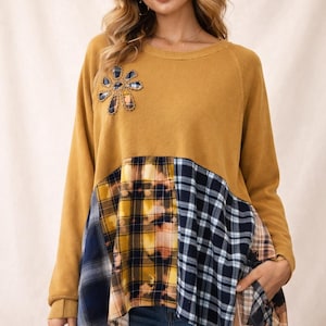 May include: Mustard yellow long-sleeve sweater with a patchwork design. The top portion is solid mustard yellow, with a floral applique. The bottom features a mix of plaid patterns in navy, yellow, and brown.
