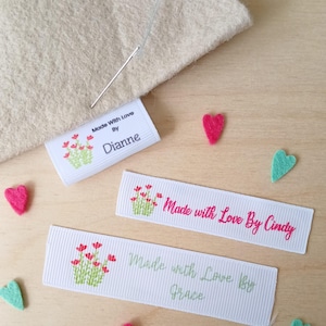 May include: Three white rectangular fabric labels with ribbed texture, each featuring a small graphic of red flowers with green stems. The labels display the text Made With Love By Dianne, Made with Love By Cindy, and Made with Love By Grace.
