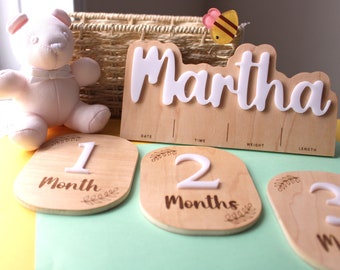 May include: A wooden baby milestone set with the name "Martha" in white letters. Includes month markers, a teddy bear, and a decorative bee. The set is designed to track baby's growth and development.