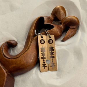 May include: Two wooden keychains with a heart-shaped cutout. Each keychain features a music note symbol and a series of lines resembling a music equalizer.