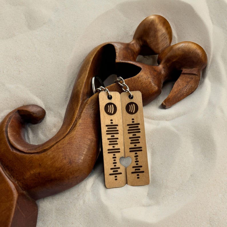May include: Two wooden keychains with a heart-shaped cutout. Each keychain features a music note symbol and a series of lines resembling a music equalizer.