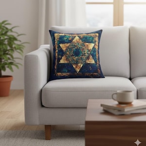 Puede incluir: Cojín decorativo cuadrado con fondo azul marino y diseño de estrella geométrica dorada y turquesa. El cojín está colocado sobre un sofá gris claro en un salón.