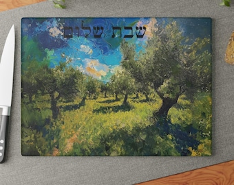 May include: A rectangular glass cutting board featuring an impressionistic painting of an olive grove under a blue sky with clouds. The Hebrew text "שבת שלום" is printed in black in the upper center of the board, which is positioned next to a knife.