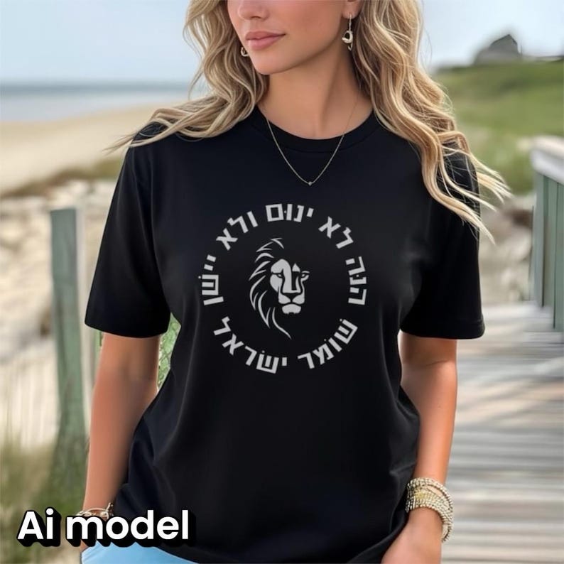 Op de afbeelding: Een zwart T-shirt met korte mouwen en een witte cirkelvormige afbeelding op de borst. Het ontwerp bevat een centrale illustratie van een leeuwenkop omringd door de Hebreeuwse tekst: הנה לא ינום ולא יישן שומר ישראל.