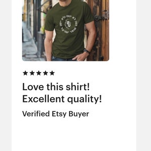 Op de afbeelding: Een olijfgroen t-shirt met korte mouwen en een cirkelvormige afbeelding op de borst. Het ontwerp bevat een centrale illustratie van een leeuwenkop omringd door Hebreeuwse tekst in een ring. Het shirt heeft een ronde hals en een standaard pasvorm.