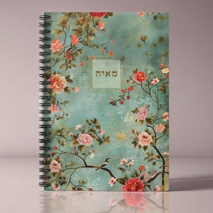 Op de afbeelding: Spiraalgebonden notitieboek met een bloemenontwerp. De omslag heeft een turquoise achtergrond met roze en rode rozen, takken en een kleine vogel. Het woord "מאיה" staat in een gouden kader.