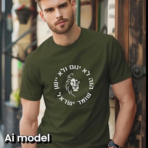 Op de afbeelding: Een olijfgroen T-shirt met korte mouwen en een witte cirkelvormige afbeelding op de borst. Het ontwerp toont een gestileerde leeuwenkop in het midden, omringd door Hebreeuwse tekst in een cirkel. De stof is van effen gebreid materiaal.