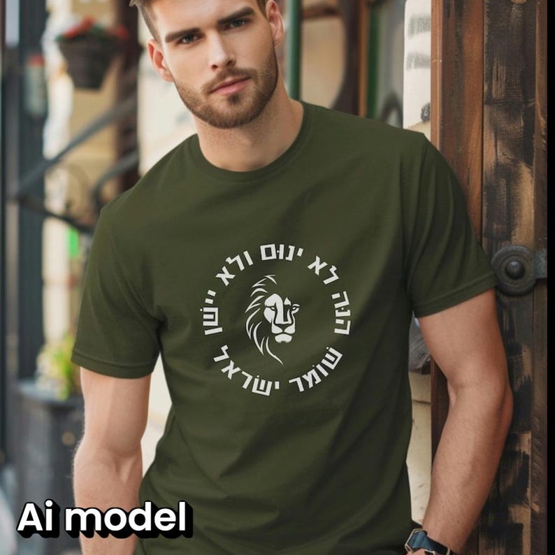 Op de afbeelding: Een olijfgroen T-shirt met korte mouwen en een witte cirkelvormige afbeelding op de borst. Het ontwerp toont een gestileerde leeuwenkop in het midden, omringd door Hebreeuwse tekst in een cirkel. De stof is van effen gebreid materiaal.