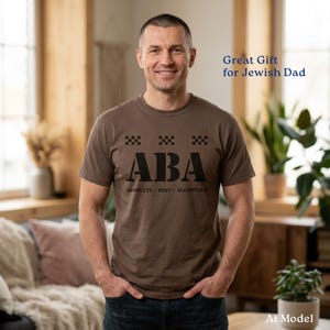 May include: A brown short-sleeved t-shirt featuring the text ABA in large black letters, with the words ABSOLUTE BEST ALGORITHM printed underneath and three small black checkered squares above the letters, centered on the chest.