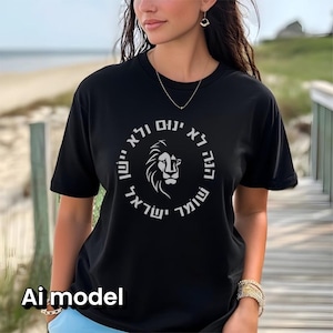 Op de afbeelding: Een zwart T-shirt met korte mouwen en een witte cirkelvormige afbeelding op de borst. Het ontwerp bevat een gestileerde leeuwenkop in het midden, omringd door Hebreeuwse tekst in een cirkel. Het shirt heeft een ronde hals en een losse pasvorm.