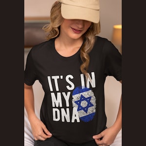 Puede incluir: Camiseta negra con texto blanco que dice "It's in my DNA" y un gráfico de huella dactilar de la bandera israelí azul y blanca.