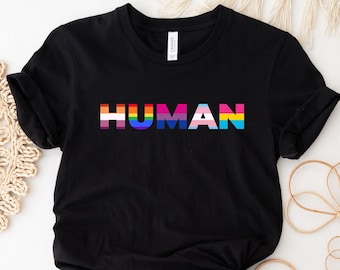 May include: Black t-shirt with the word "HUMAN" printed in rainbow colors, representing the LGBTQ+ pride flag.