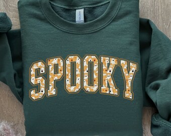 May include: A dark green sweatshirt with the word "SPOOKY" printed in yellow letters. The letters are filled with a pattern of white ghosts with orange faces.