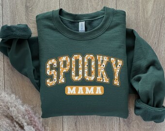 May include: A dark green sweatshirt with a gold and white graphic that says "Spooky Mama" with a pattern of ghosts and pumpkins.