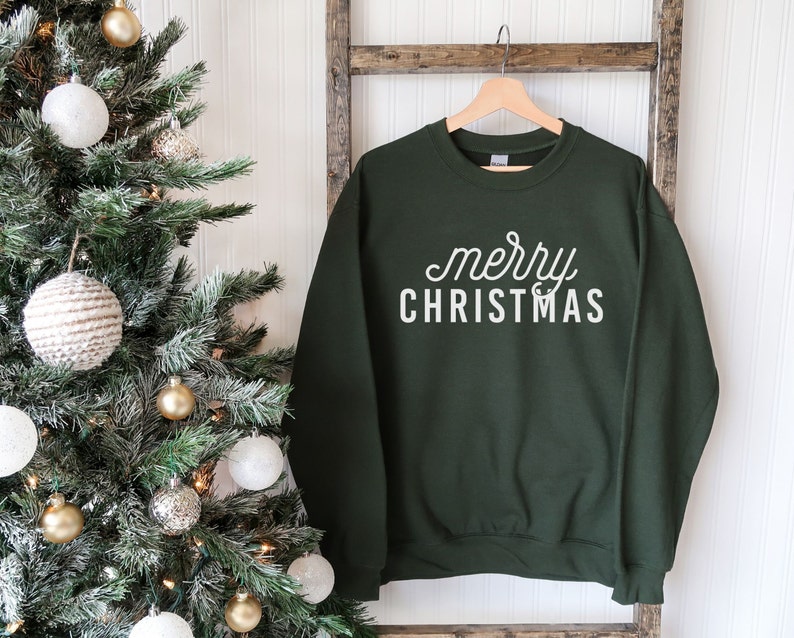 Op de afbeelding: Een donkergroen sweatshirt met de tekst "merry christmas" in witte letters.