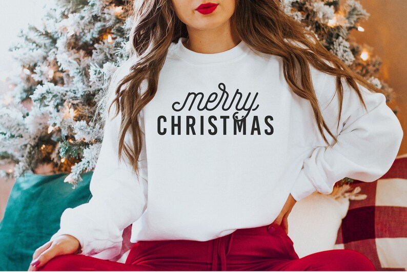Op de afbeelding: Witte trui met de tekst "merry CHRISTMAS" in zwarte letters.