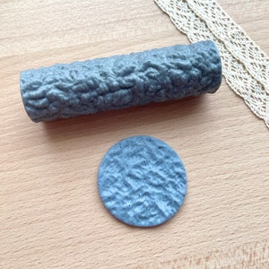 Könnte beinhalten: Ein Set aus zwei grauen, strukturierten Silikon-Nudelholzern zum Backen. Das größere Nudelholz ist zylindrisch und das kleinere ist rund.