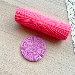 May include: A pink silicone rolling pin and a purple silicone mold with a sunburst design. Both tools are used for decorating cakes and pastries.