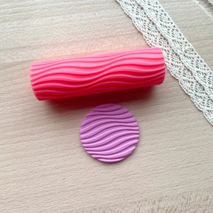 Pode incluir: Um rolo de silicone rosa com um padrão ondulado e um círculo de silicone roxo correspondente com o mesmo padrão ondulado.