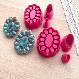 May include: Two sets of pink plastic cookie cutters in the shape of a large oval with smaller ovals around the edge. The cutters are used to create turquoise and brown jewelry.