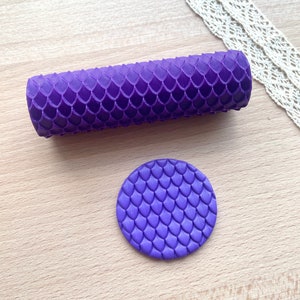 Op de afbeelding: Paarse deegroller en een ronde afdruktool met een draken schubbenpatroon.