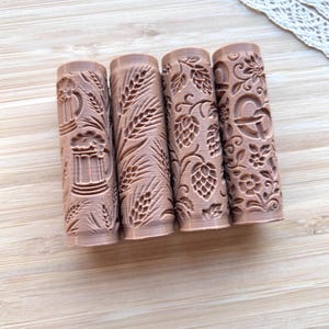Peut inclure: Quatre rouleaux à pâtisserie cylindriques brun clair avec des motifs en relief. Le premier montre des chopes de bière et du blé, le deuxième des épis de blé, le troisième des cônes de houblon et le quatrième un bretzel avec des fleurs.