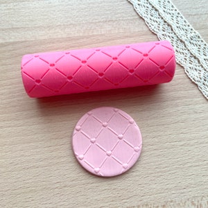 May include: A bright pink cylindrical rolling pin featuring a raised diamond grid pattern with small hearts at each intersection, accompanied by a light pink circular disc embossed with the identical matching diamond and heart design.