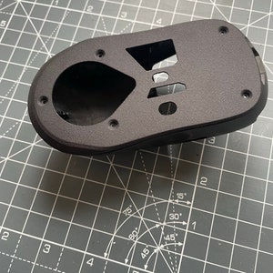 May include: A black plastic mouse shell with a textured surface. The shell has several holes and a large opening in the center.