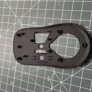 May include: Black plastic mouse shell with multiple holes and a textured surface. The shell is designed for a computer mouse.
