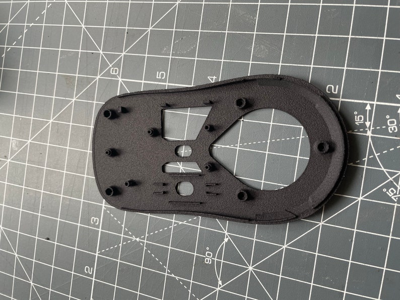 May include: Black plastic mouse shell with multiple holes and a textured surface. The shell is designed for a computer mouse.