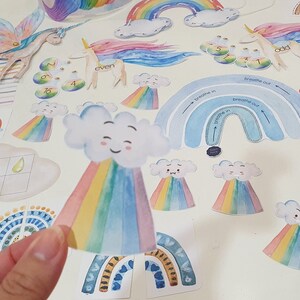 May include: A set of colorful rainbow-themed educational craft supplies for kids. The set includes a rainbow with a cloud, a rainbow with a smiling face, and a rainbow with the words "breathe in" and "breathe out".