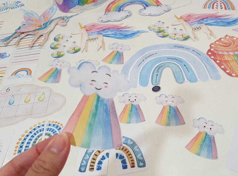May include: A set of colorful rainbow-themed educational craft supplies for kids. The set includes a rainbow with a cloud, a rainbow with a smiling face, and a rainbow with the words "breathe in" and "breathe out".