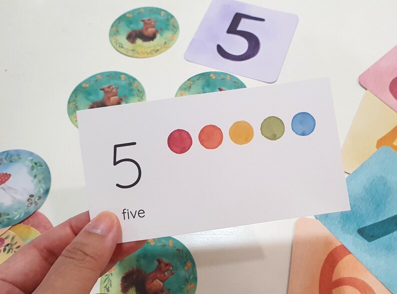 May include: A white card with the number 5 and the word "five" written on it. There are five colored dots in a row across the card: red, orange, yellow, green, and blue.