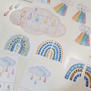 May include: A set of colorful rainbow and raindrop themed educational cards for children. The cards feature different patterns and designs, including polka dots, stripes, and geometric shapes. The cards also include numbers and counting activities.