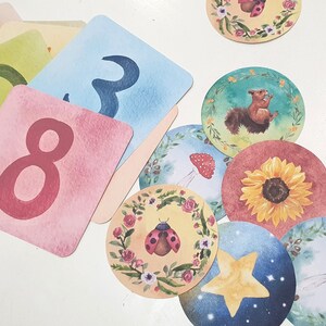 May include: A set of colorful cards with numbers and illustrations. The cards feature a ladybug, a sunflower, a squirrel, a mushroom, and a star. The cards are perfect for learning to count and for playing games.