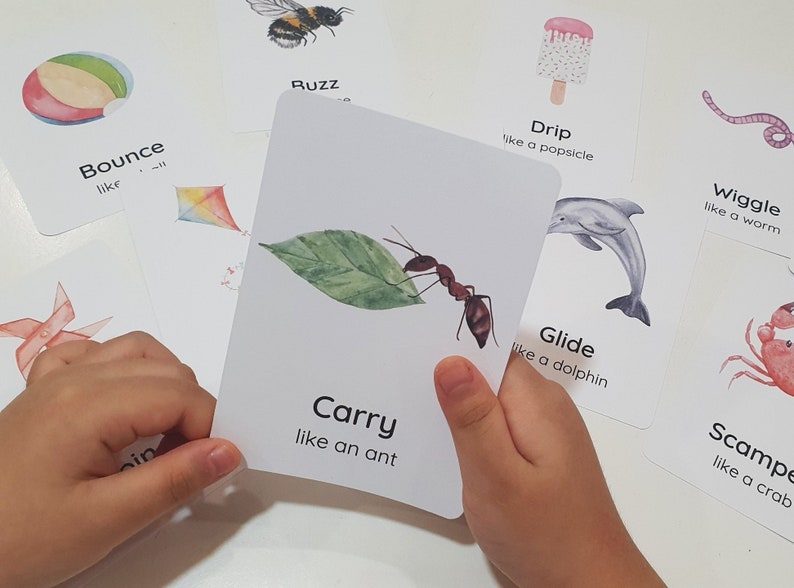 May include: Educational flashcards with watercolor illustrations. One card shows an ant carrying a leaf, with the word "Carry" and the phrase "like an ant." Other cards show a bee, a popsicle, a worm, a dolphin, and a crab.