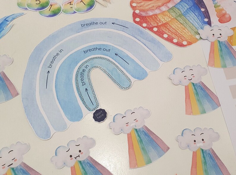 May include: A blue and white rainbow with the words "breathe in" and "breathe out" written on it. There are also several small clouds with rainbows underneath them. The clouds have happy faces on them. The words "Start here" are written on a small circle.