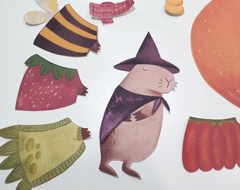 May include: A set of colorful felt cutouts for a craft project. The cutouts include a strawberry, a bee, a pumpkin, a capybara wearing a witch's hat, a scarf, and a paw print.