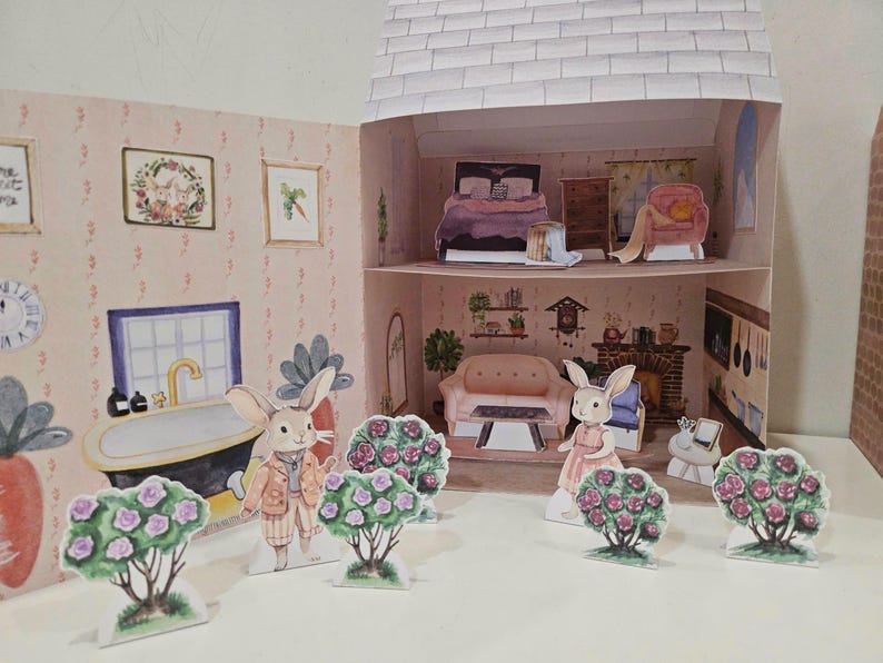 May include: A paper dollhouse with a pink and white exterior. The dollhouse has two floors and is decorated with flowers and a clock. There are two bunny paper dolls standing in front of the dollhouse.