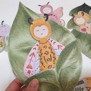 May include: A set of five paper cut-out butterflies with floral patterns and green leaves. The butterflies are in various colors, including pink, yellow, and blue. The butterflies are arranged in a cluster, with the leaves surrounding them.